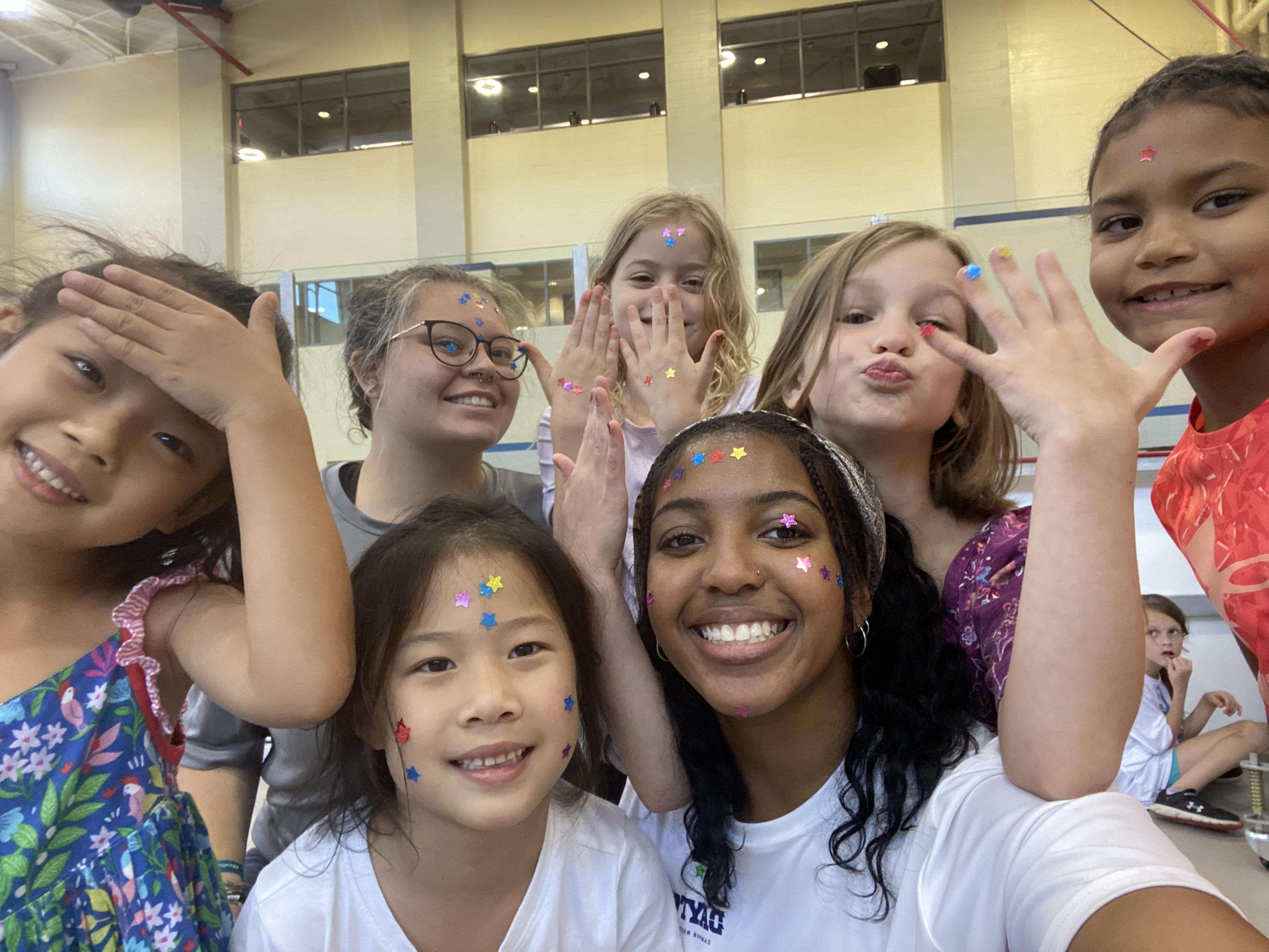 A selfie with a Camp counselor and a group of young campers showing off their stickers from an activity they did.