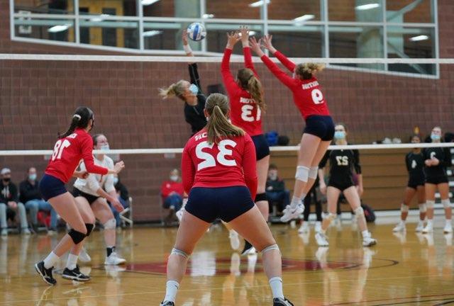 Two students block a hit in a women's club volleyball game. 